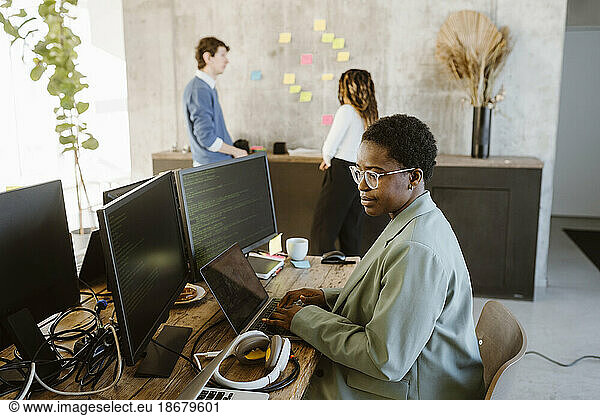 Side view of female programmer working on computer at desk in creative office