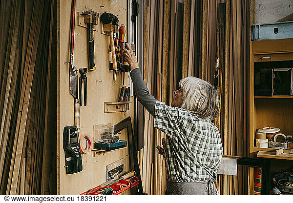 Side view of female senior carpenter removing tool from board at workshop