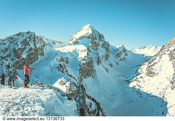 Side view of female skier standing against snowcapped mountains