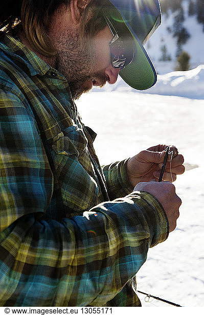 Side view of fisherman preparing fishing rod on snowy field