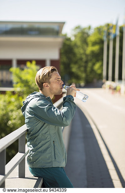 Side view of fit man drinking water on bridge