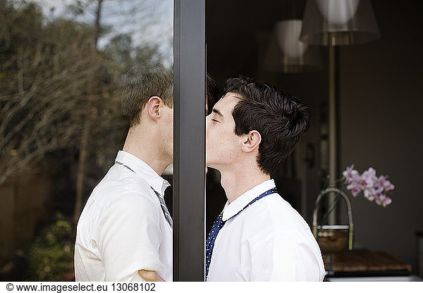 Side view of gay couple kissing while standing at doorway