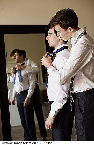 Side view of gay man assisting boyfriend for tying necktie