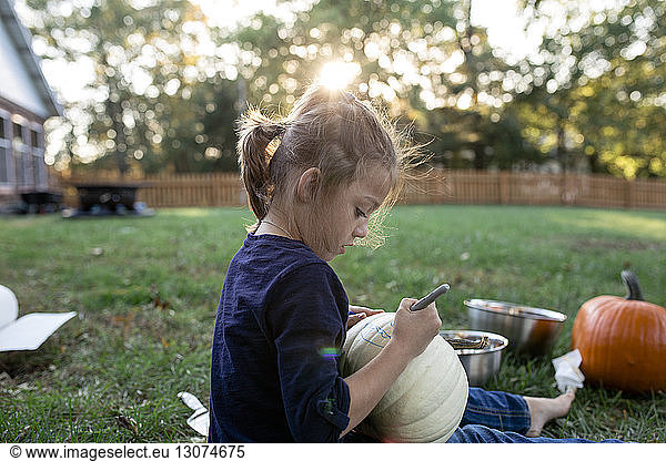 Side view of girl carving pumpkin while sitting in yard during Halloween