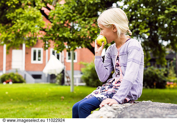 Side view of girl eating apple in yard