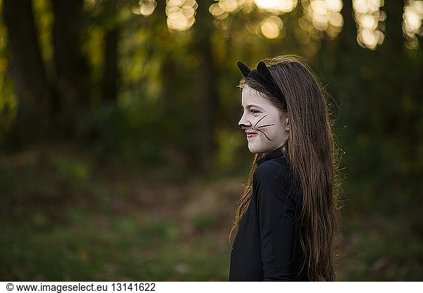 Side view of girl in face paint standing at park during sunset