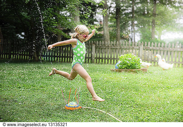 Side view of girl in swimwear running over sprinklers at yard