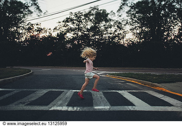 Side view of girl jumping on zebra crossing against trees