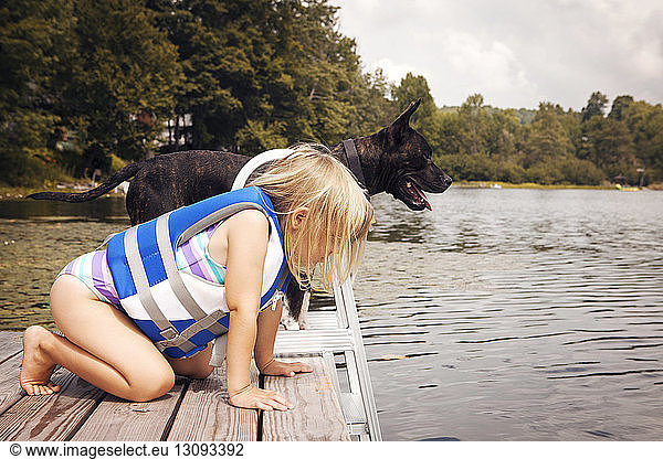 Side view of girl looking down while kneeling by dog on pier