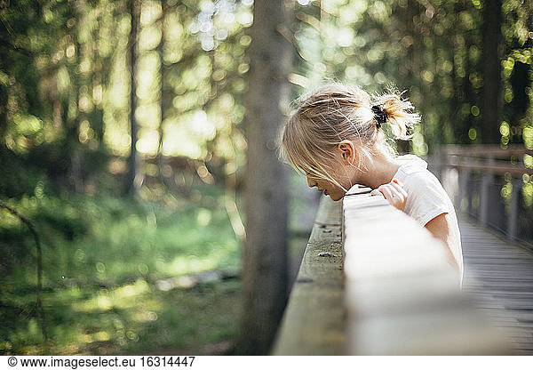 Side view of girl looking down while standing on footbridge in forest