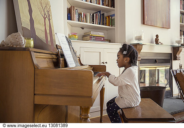 Side view of girl playing piano in living room