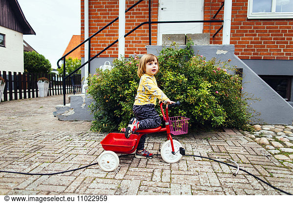 Side view of girl riding tricycle outside house