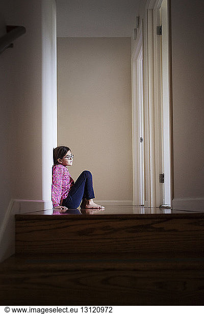 Side view of girl sitting on floor by wall at home
