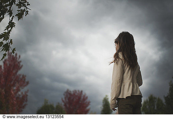 Side view of girl standing against cloudy sky