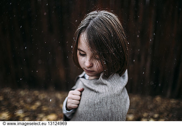 Side view of girl standing at backyard during snowfall