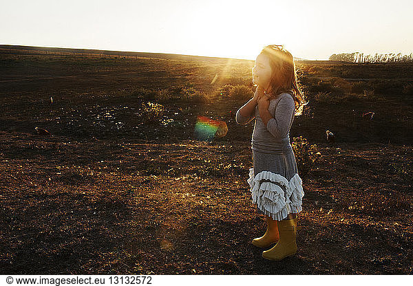 Side view of girl standing on field against sky during sunset
