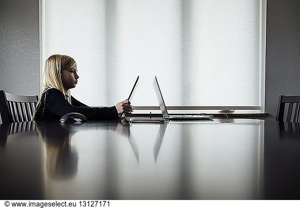 Side view of girl using laptop computer while sitting at home