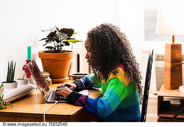 Side view of girl using laptop while sitting at table in living room