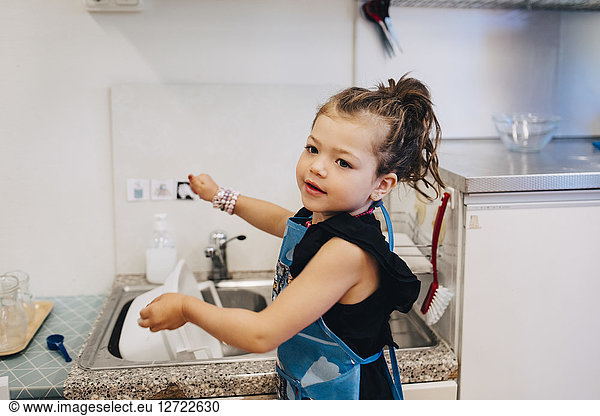 Side view of girl washing utensil in sink at child care