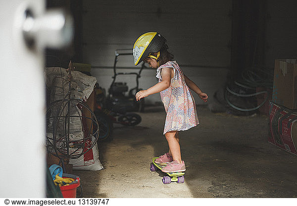 Side view of girl wearing helmet while standing on skateboard in garage