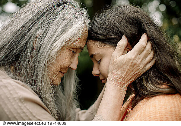 Side view of grandmother and granddaughter touching heads with eyes closed