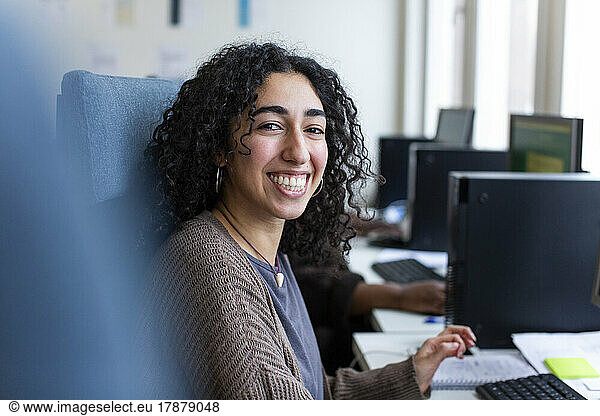 Side view of happy businesswoman sitting at desk in office