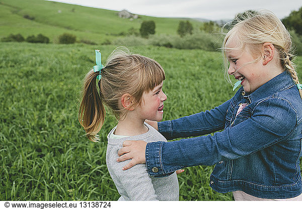 Side view of happy sisters looking at each other while standing on grassy field