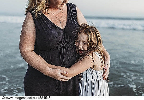 Side view of happy young daughter hugging mother in ocean at dusk