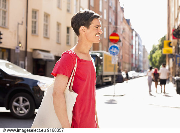 Side view of happy young man with bag walking on city street