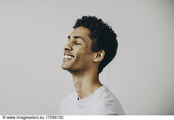 Side view of happy young man with eyes closed against white background
