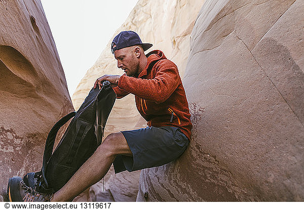Side view of hiker looking into backpack while leaning amidst canyons