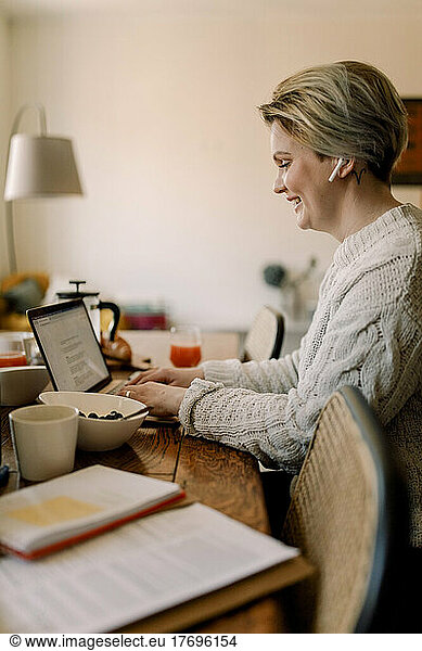 Side view of lesbian businesswoman using laptop sitting at dining table