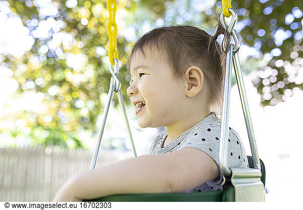 Side View of Little Girl Sitting in Backyard Swing Lächeln