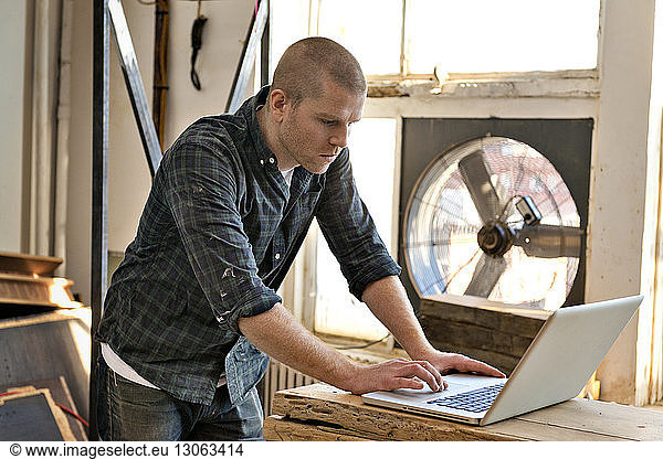 Side view of male carpenter using laptop in workshop