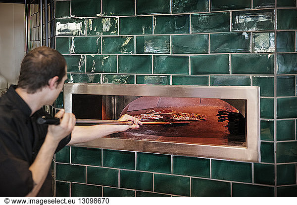 Side view of male chef placing pizzas in oven at commercial kitchen