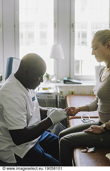Side view of male doctor checking blood sugar level of patient sitting in clinic