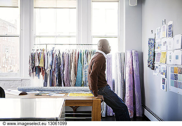 Side view of male fashion designer looking at designs on wall in workshop