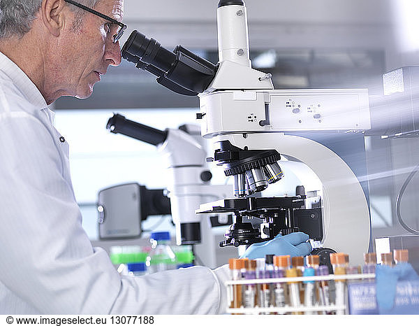 Side view of male scientist analyzing blood samples through microscope in laboratory