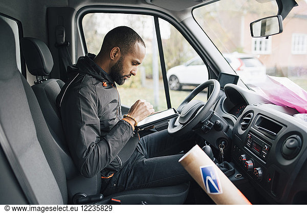 Side view of male worker using digital tablet while sitting in delivery van