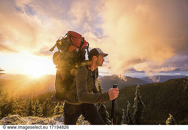 Side view of man backpacking on mountain ridge with scenic view.