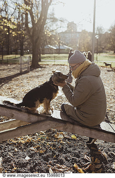 Side view of man bonding with dog while sitting at park during autumn