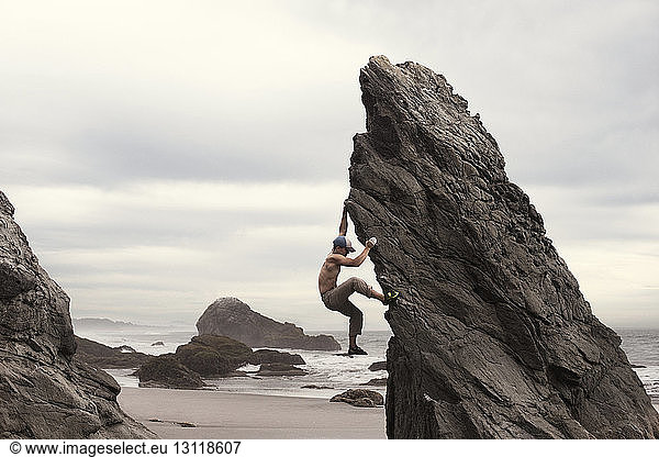 Side view of man climbing rock formation at beach