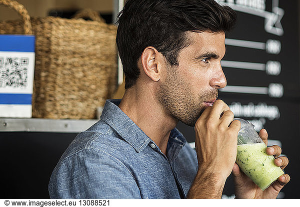 Side view of man drinking smoothie while standing by food truck