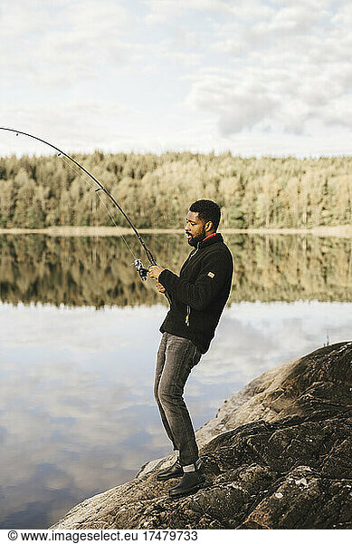 Side view of man fishing while standing on rock