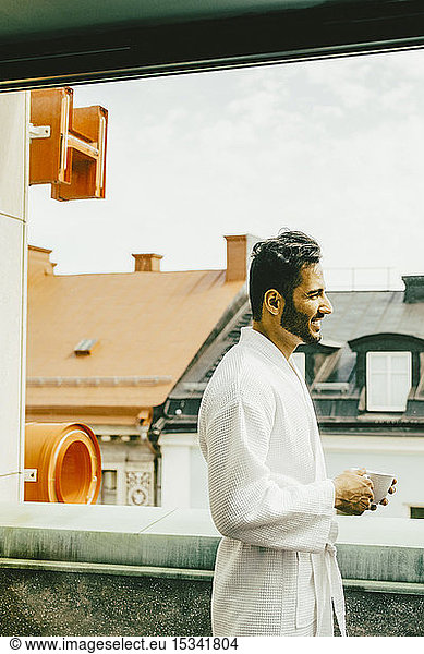 Side view of man holding coffee cup standing in hotel balcony