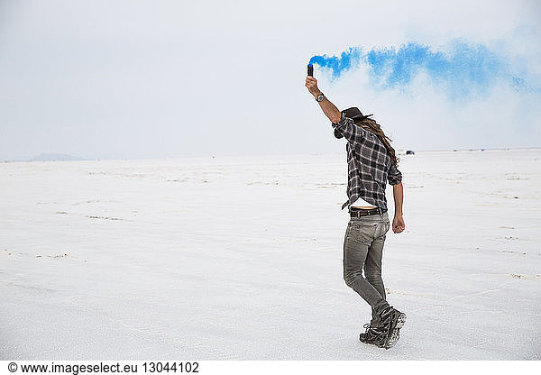 Side view of man holding smoke bomb while standing on Bonneville Salt Flats against sky