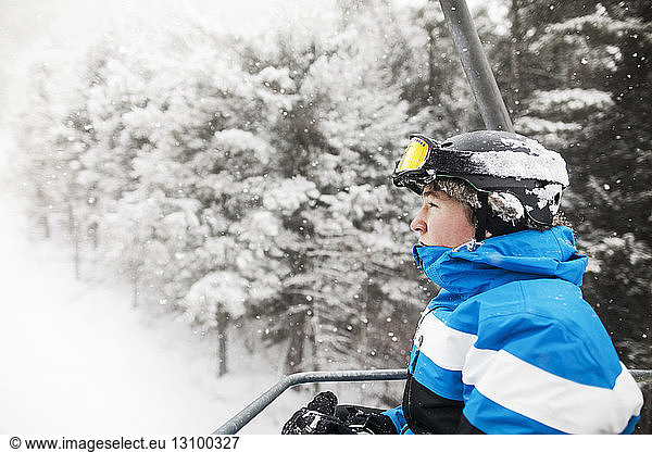 Side view of man in ski lift against snow covered trees