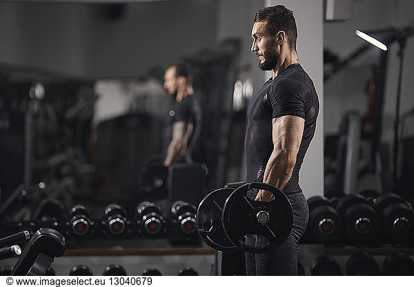 Side view of man lifting barbell while exercising at gym