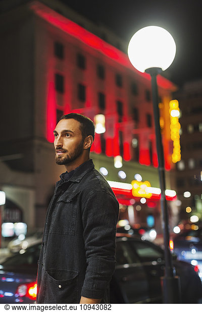 Side view of man looking away while standing in city at night