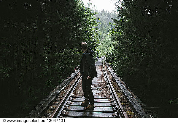 Side view of man looking over shoulder on railway tracks amidst trees